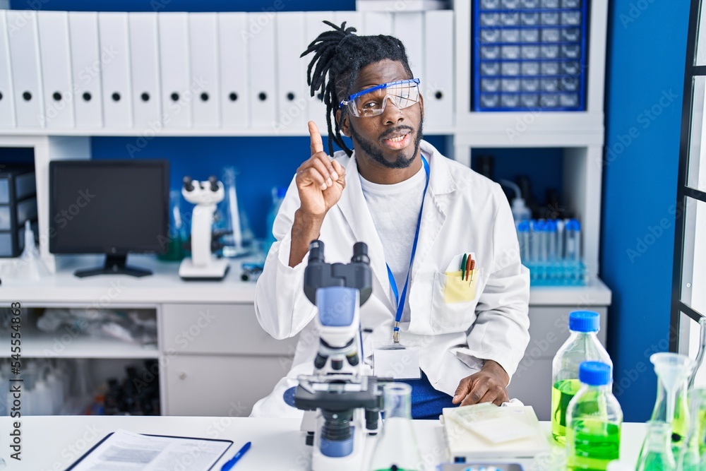 African man with dreadlocks working at scientist laboratory smiling with an idea or question pointing finger up with happy face, number one African man with dreadlocks working at scientist laboratory smiling with an idea or question pointing finger up with happy face, number one