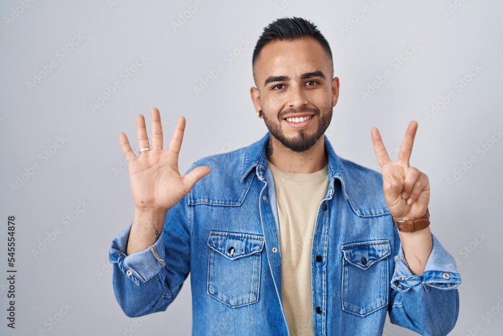 Young hispanic man standing over isolated background showing and pointing up with fingers number seven while smiling confident and happy. Young hispanic man standing over isolated background showing and pointing up with fingers number seven while smiling confident and happy.