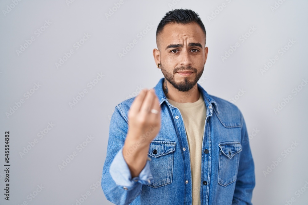 Young hispanic man standing over isolated background doing italian gesture with hand and fingers confident expression Young hispanic man standing over isolated background doing italian gesture with hand and fingers confident expression