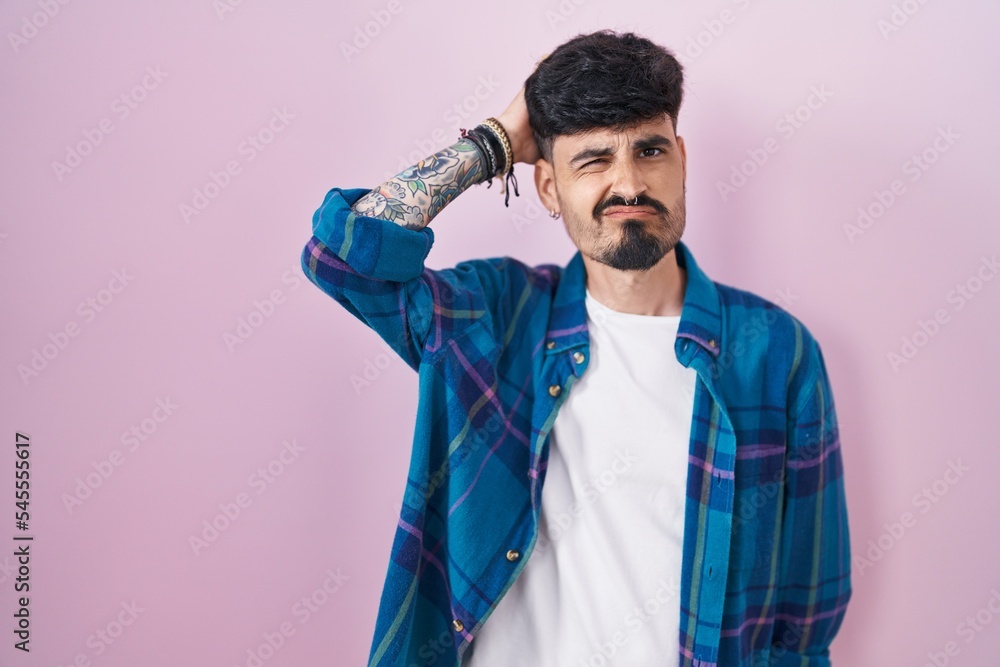 Young hispanic man with beard standing over pink background confuse and wonder about question. uncertain with doubt, thinking with hand on head. pensive concept. Young hispanic man with beard standing over pink background confuse and wonder about question. uncertain with doubt, thinking with hand on head. pensive concept.