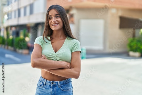 Young beautiful hispanic woman standing with arms crossed gesture at street