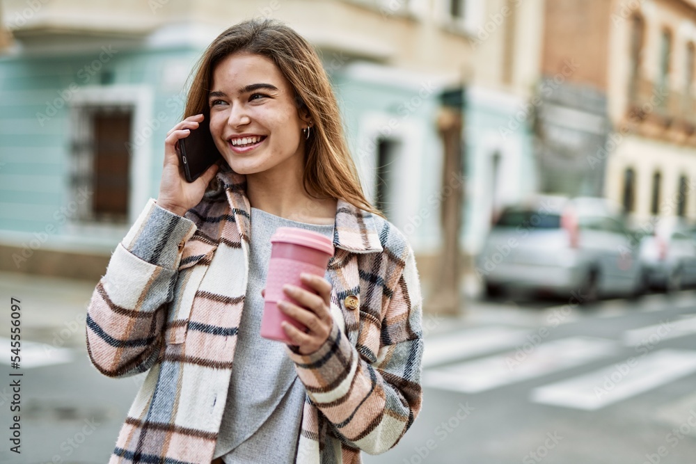 Young blonde woman holding coffee talking on the smartphone at street Young blonde woman holding coffee talking on the smartphone at street