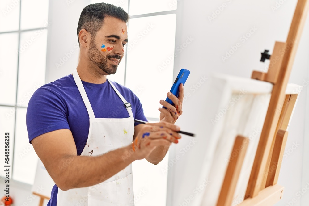Young hispanic man smiling confident drawing using smartphone at art studio