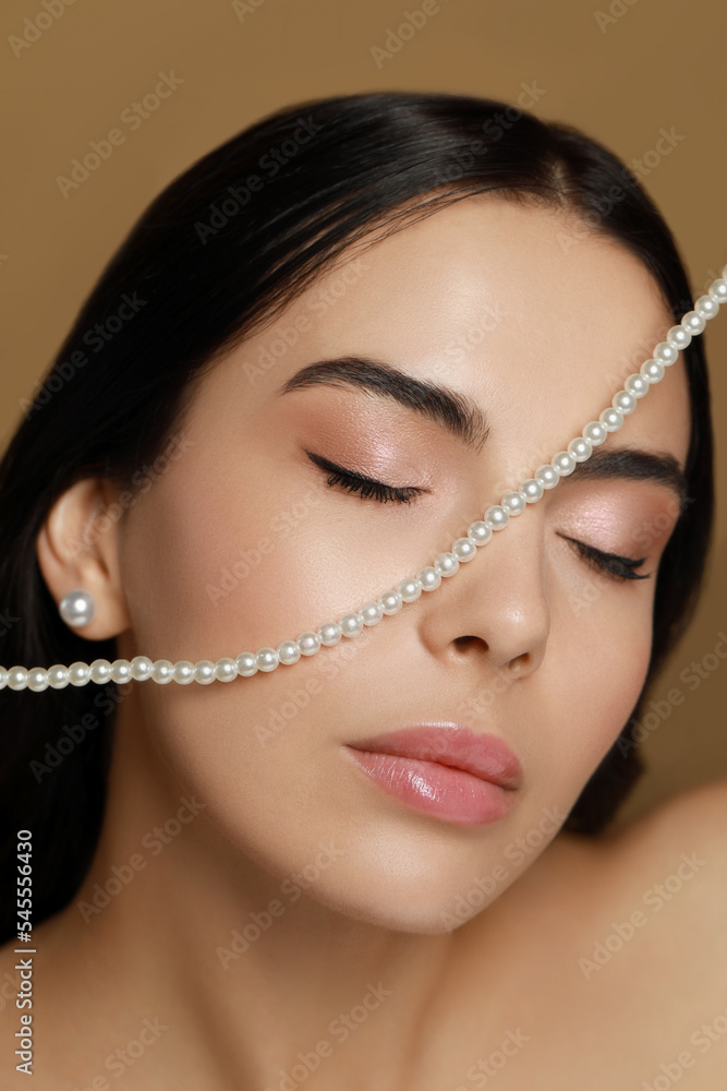 Young woman with elegant pearl jewelry on brown background, closeup