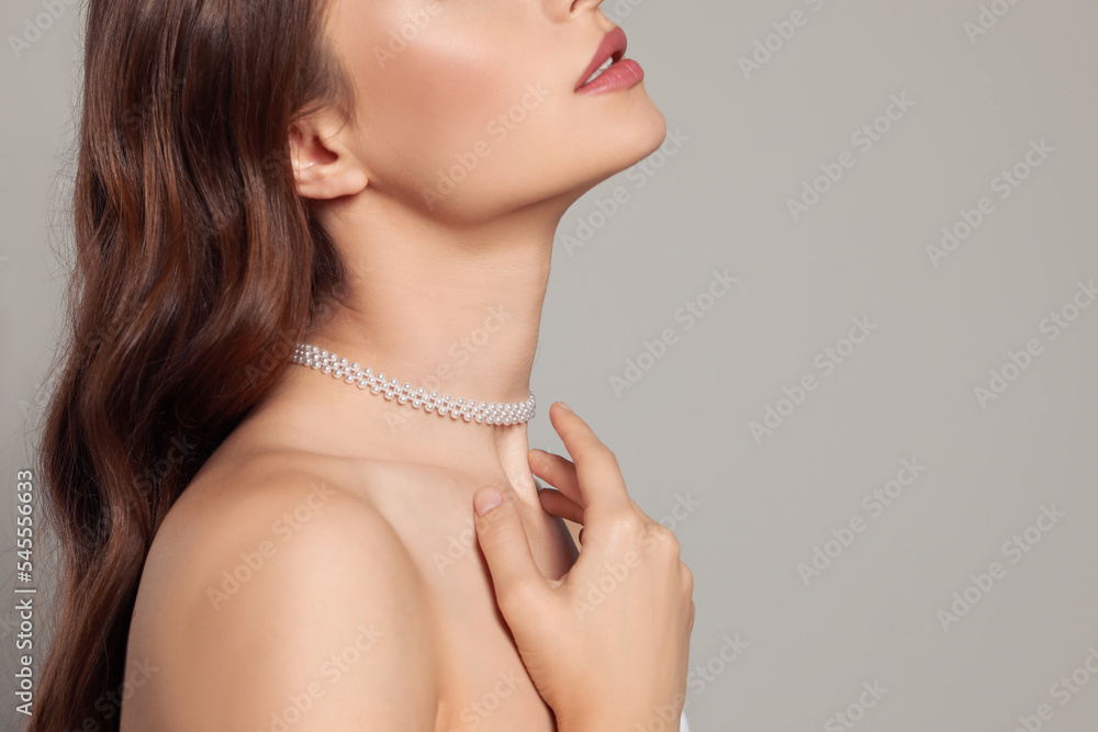 Young woman wearing elegant pearl necklace on grey background, closeup. Space for text