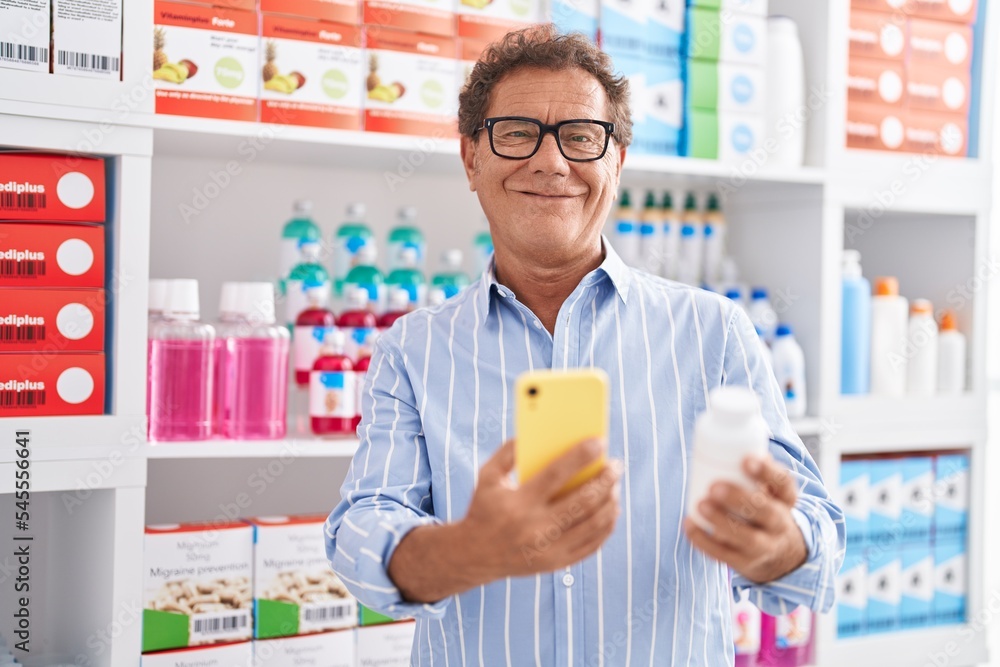 Middle age man customer using smartphone holding pills bottle at pharmacy Middle age man customer using smartphone holding pills bottle at pharmacy