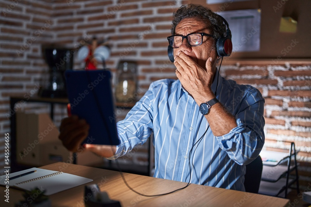 Middle age hispanic man using touchpad sitting on the table at night bored yawning tired covering mouth with hand. restless and sleepiness. Middle age hispanic man using touchpad sitting on the table at night bored yawning tired covering mouth with hand. restless and sleepiness.