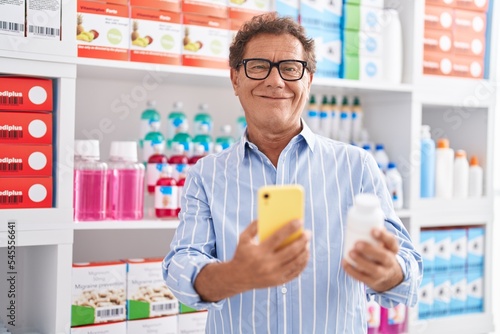 Middle age man customer using smartphone holding pills bottle at pharmacy