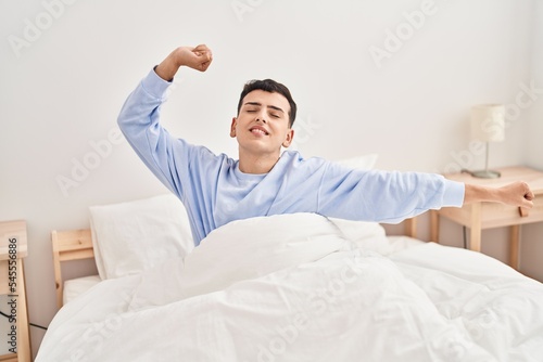 Young non binary man waking up stretching arms