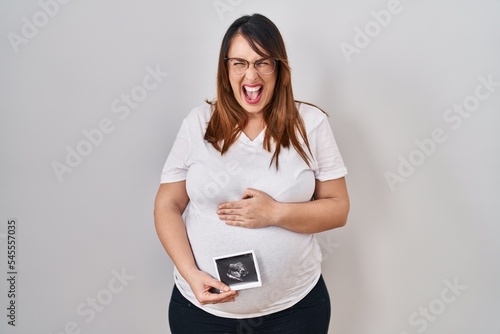 Pregnant woman holding baby ecography angry and mad screaming frustrated and furious, shouting with anger. rage and aggressive concept.