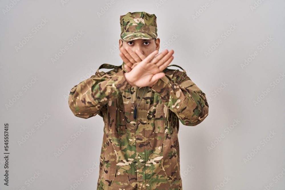 Young arab man wearing camouflage army uniform rejection expression crossing arms and palms doing negative sign, angry face Young arab man wearing camouflage army uniform rejection expression crossing arms and palms doing negative sign, angry face