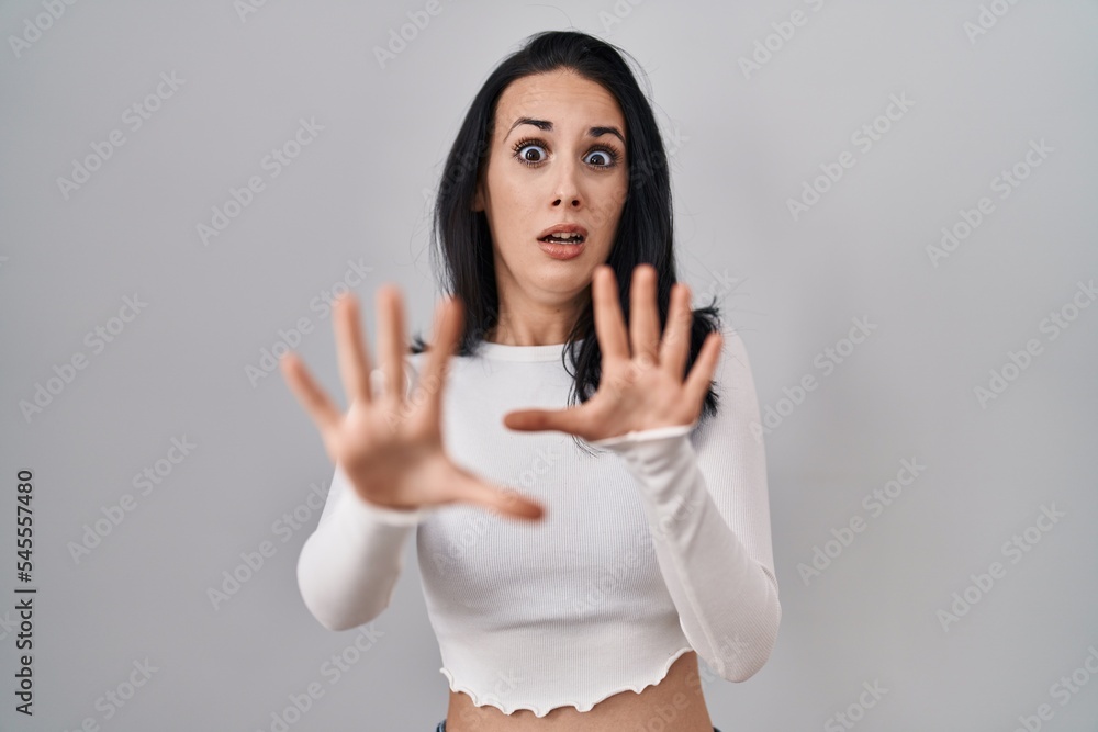 Hispanic woman standing over isolated background afraid and terrified with fear expression stop gesture with hands, shouting in shock. panic concept. Hispanic woman standing over isolated background afraid and terrified with fear expression stop gesture with hands, shouting in shock. panic concept.