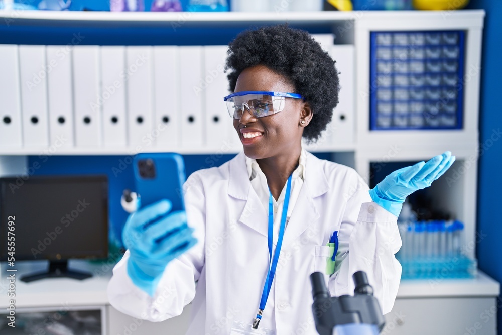 African young woman working at scientist laboratory doing video call celebrating achievement with happy smile and winner expression with raised hand African young woman working at scientist laboratory doing video call celebrating achievement with happy smile and winner expression with raised hand