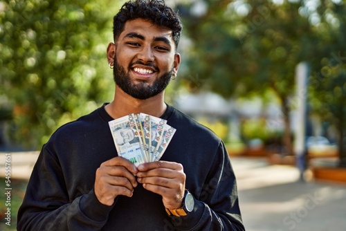 Young arab man smiling confident holding sol peruvian banknotes at park photo
