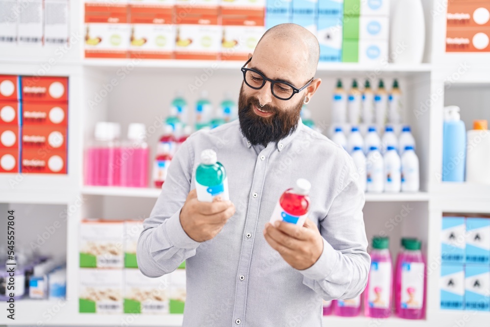 Young bald man customer smiling confident holding medication bottles at pharmacy