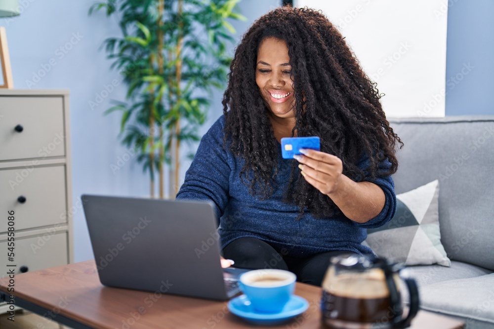 African american woman using laptop and credit card sitting on sofa at home African american woman using laptop and credit card sitting on sofa at home