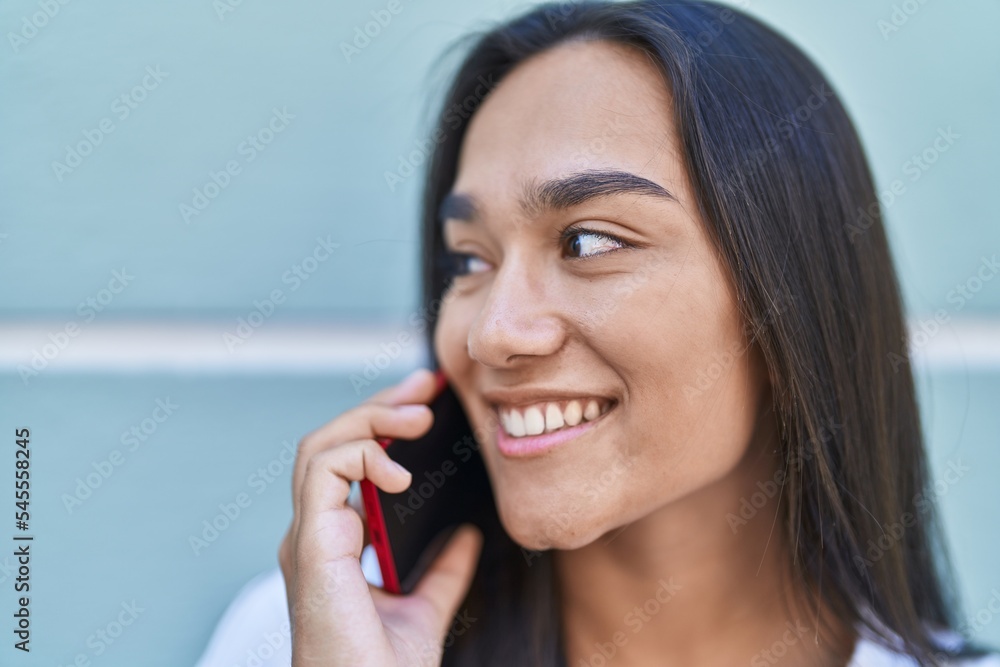 Young beautiful hispanic woman smiling confident talking on the smartphone over isolated blue wall background Young beautiful hispanic woman smiling confident talking on the smartphone over isolated blue wall background