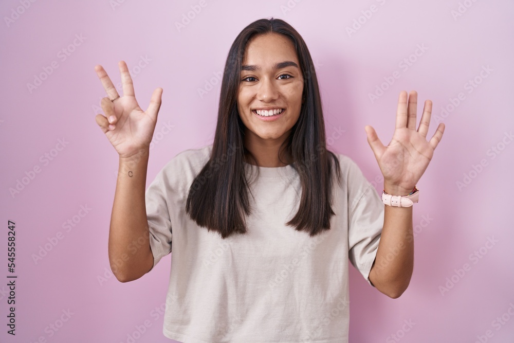 Young hispanic woman standing over pink background showing and pointing up with fingers number eight while smiling confident and happy. Young hispanic woman standing over pink background showing and pointing up with fingers number eight while smiling confident and happy.