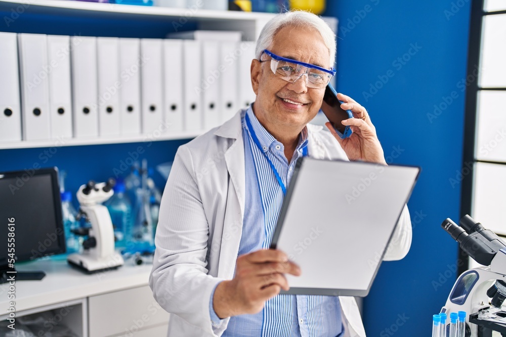 Senior man scientist talking on the smartphone writing on document at laboratory Senior man scientist talking on the smartphone writing on document at laboratory