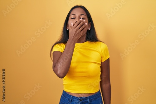Young indian woman standing over yellow background bored yawning tired covering mouth with hand. restless and sleepiness. © Krakenimages.com
