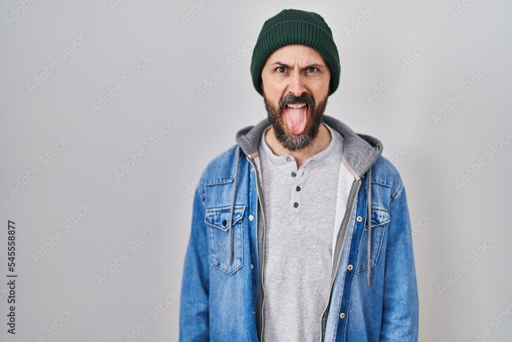Young hispanic man with tattoos wearing wool cap sticking tongue out happy with funny expression. emotion concept. Young hispanic man with tattoos wearing wool cap sticking tongue out happy with funny expression. emotion concept.