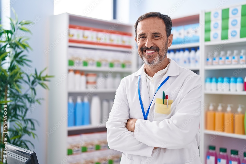Middle age man pharmacist smiling confident standing with arms crossed gesture at pharmacy Middle age man pharmacist smiling confident standing with arms crossed gesture at pharmacy
