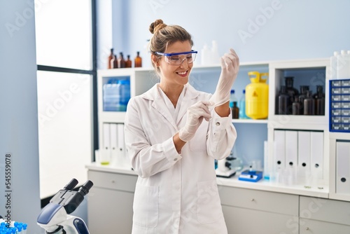 Young blonde woman wearing scientist uniform and gloves at laboratory