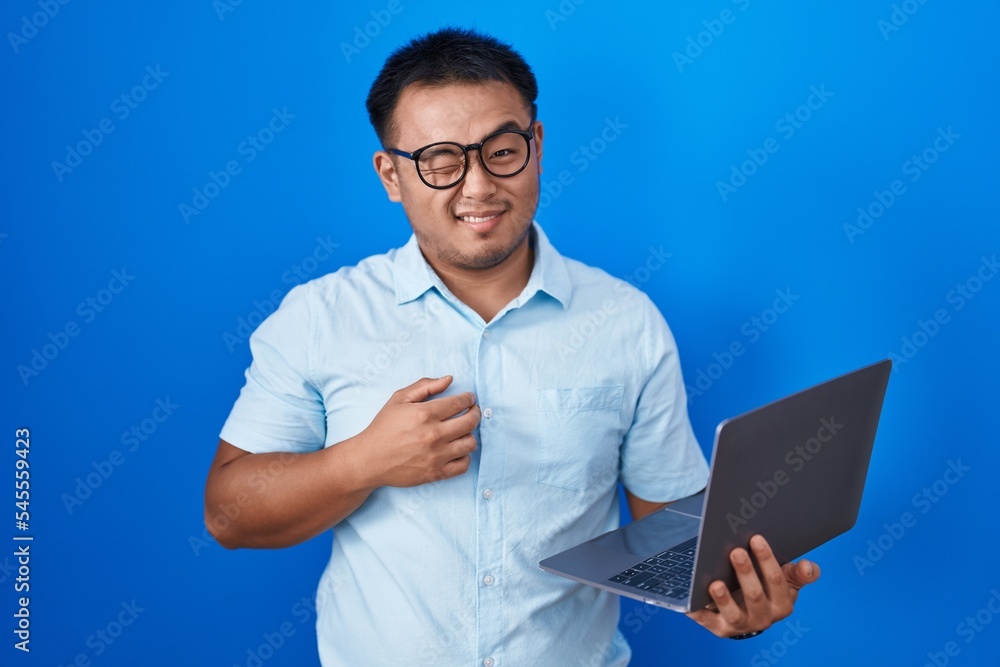 Chinese young man using computer laptop winking looking at the camera with sexy expression, cheerful and happy face. Chinese young man using computer laptop winking looking at the camera with sexy expression, cheerful and happy face.