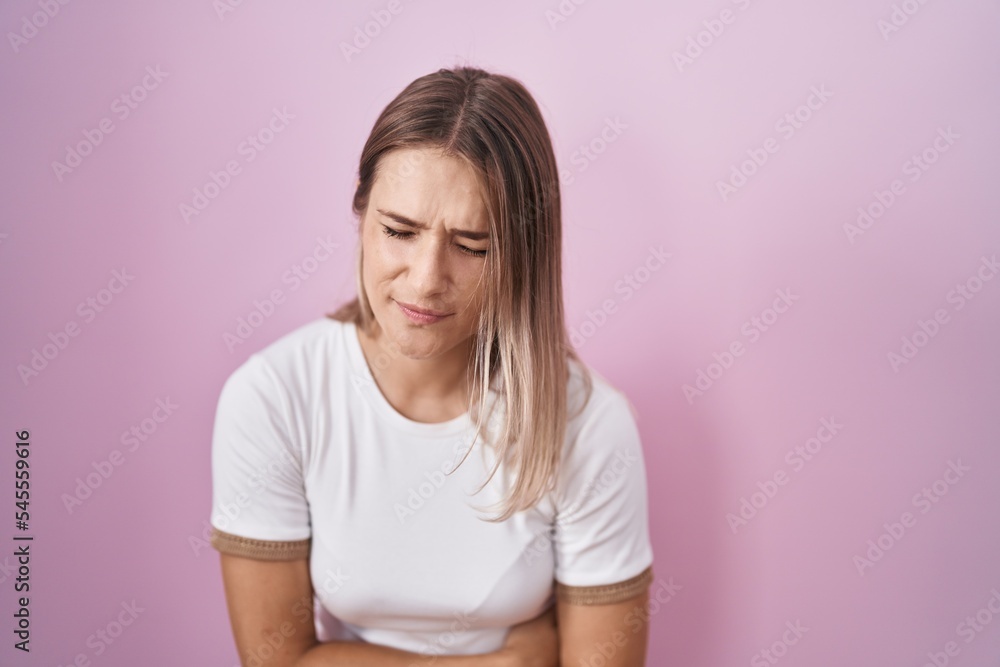 Blonde caucasian woman standing over pink background with hand on stomach because indigestion, painful illness feeling unwell. ache concept. Blonde caucasian woman standing over pink background with hand on stomach because indigestion, painful illness feeling unwell. ache concept.