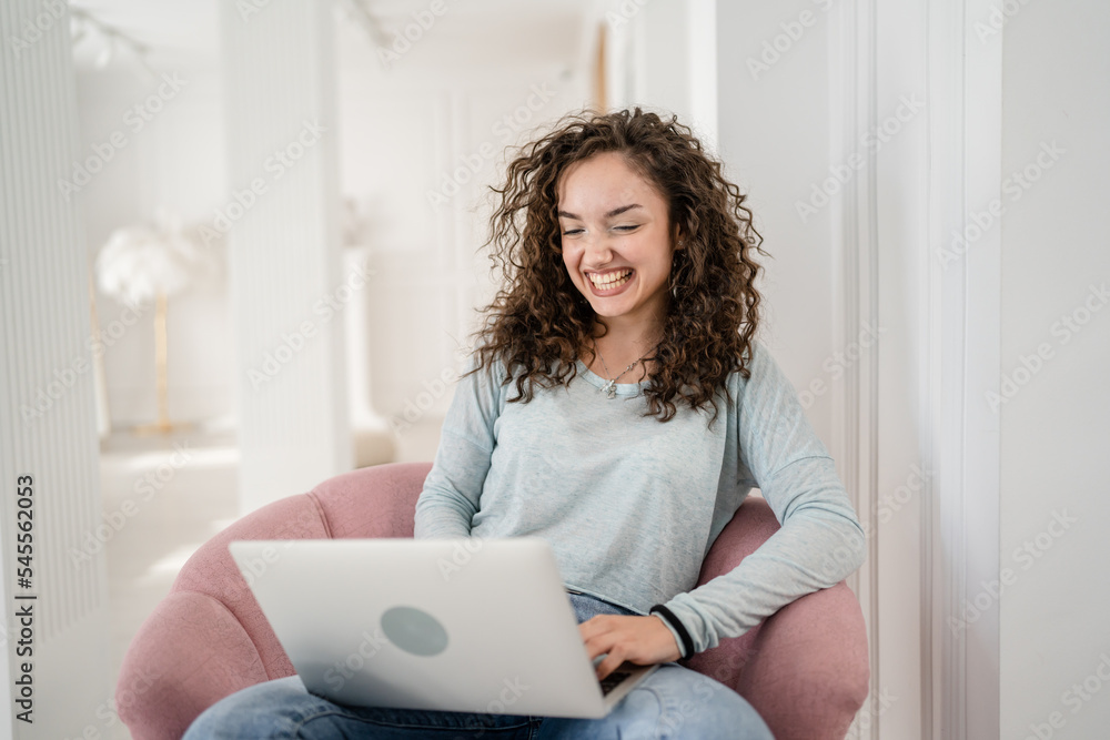 One young adult woman using laptop computer while sit in chair at home One young adult woman using laptop computer while sit in chair at home