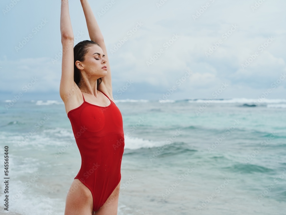 Sexy woman in red swimsuit on the ocean beach with wet hair does yoga, slim pumped body sunscreen Sexy woman in red swimsuit on the ocean beach with wet hair does yoga, slim pumped body sunscreen