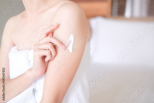 Asia woman sitting on bed and applying cream on arm
