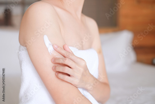 Asia woman sitting on bed and applying cream on arm