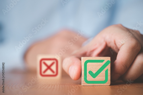 Businessman select green correct sign mark between Red Cross mark which print screen on wooden cube block for approve and reject business proposal concept. photo