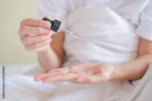 Asia woman sitting on bed and applying serum on Hand.