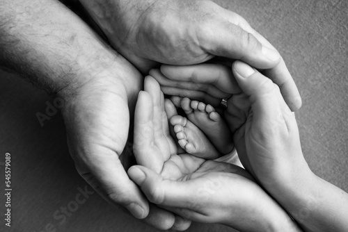 Children's foot in the hands of mother, father, parents. Feet of a tiny newborn close up. Little baby legs. Mom and her child. Happy family concept. Black and white image of motherhood stock photo.