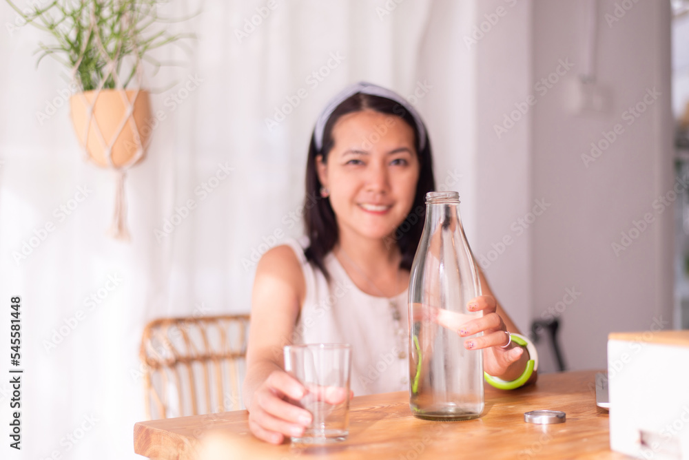Blured of woman hands holding purified fresh water in glass bottle on the table,Concept of drinking water and your health Blured of woman hands holding purified fresh water in glass bottle on the table,Concept of drinking water and your health