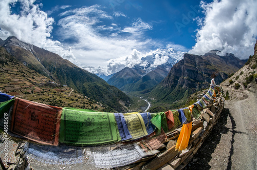 Tibetan prayer flags strung along a Mani wall of carved prayer stone, on the side of the road with view of Annapurna IV (7,525 m) Ghyaru Village, Annapurna Region, Nepal photo
