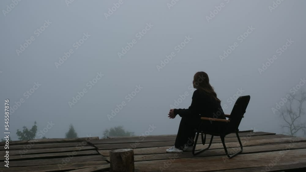 A young woman sitting on the chair and looking at the nature view with cloudy sky A young woman sitting on the chair and looking at the nature view with cloudy sky