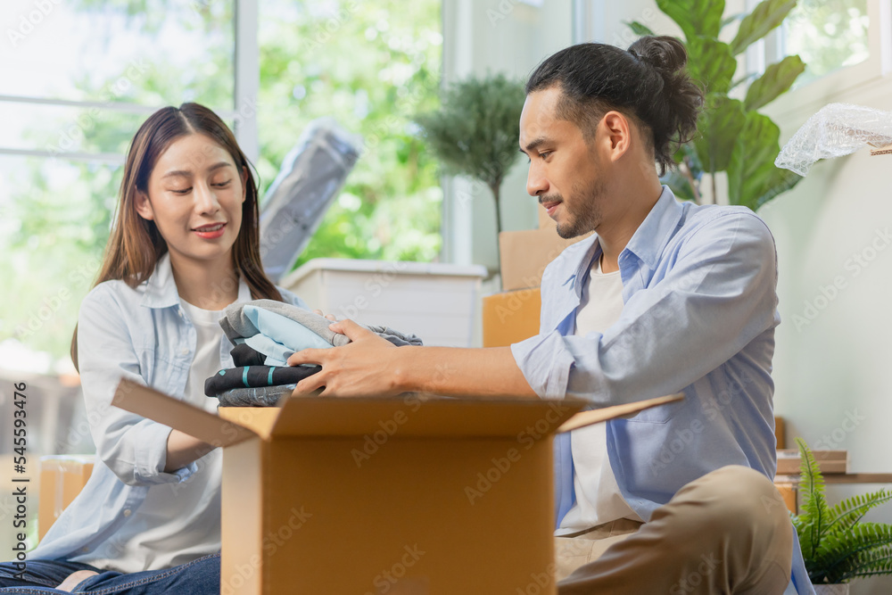 Obraz premium Happy couple asian young woman, man.packing stuff clothes, give second hand for donate, check list object in cardboard box. Moving, preparing in new home, apartment relocation. Mortgage, real estate.