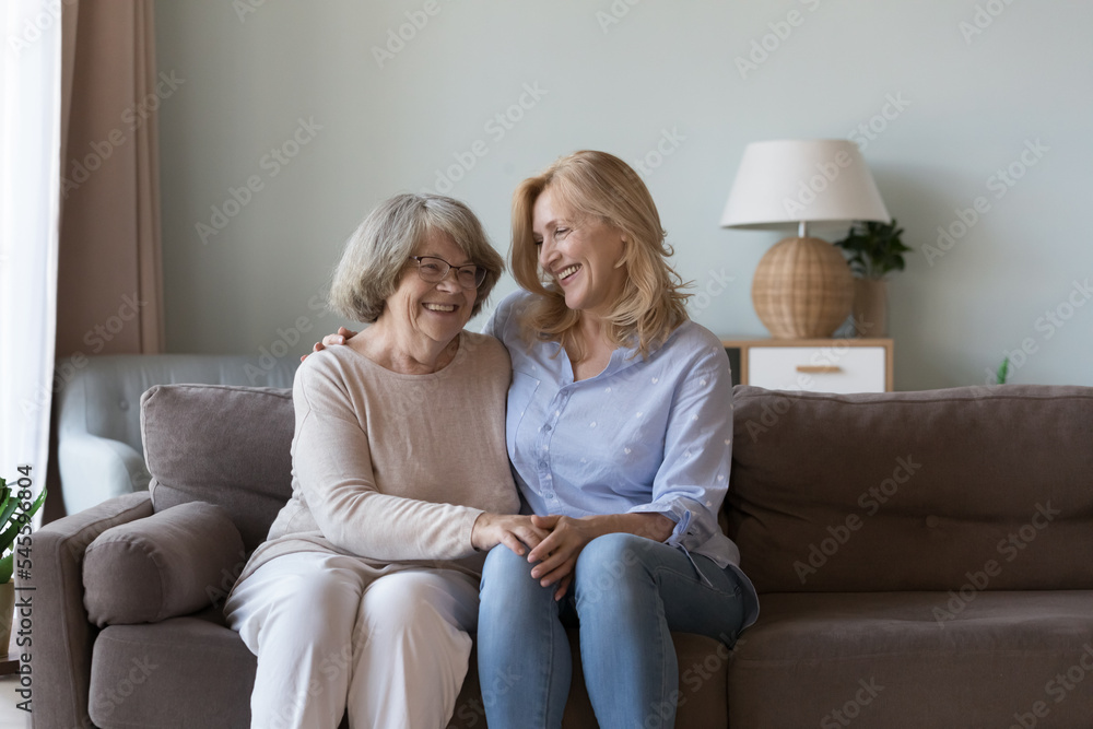 Middle-aged woman visit old mother, multi-generational family sit on sofa smile enjoy warm conversation and priceless time together. Harmony, communication between different generation relatives women