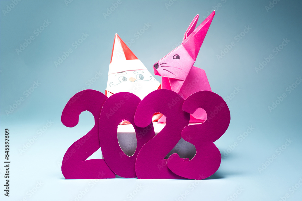 Fototapeta premium Blue background with numbers 2023, cheerful Santa claus and pink rabbit close-up