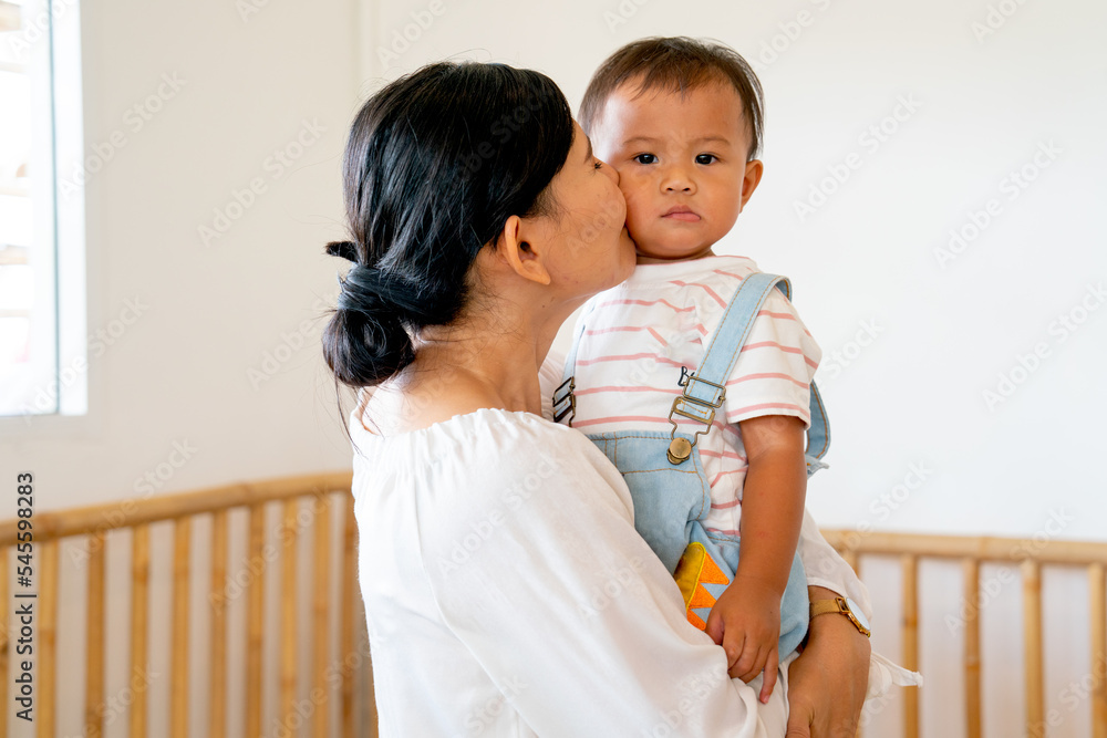 Asian mother carry and kiss her little boy and child look at camera and they stay in nursery or school in concept of good relationship and love bonding in family. Asian mother carry and kiss her little boy and child look at camera and they stay in nursery or school in concept of good relationship and love bonding in family.