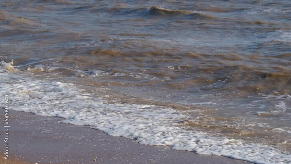 Muddy surf waves. Yellow-brown muddy surf waves with white foam, beating on the shore close-up Muddy surf waves. Yellow-brown muddy surf waves with white foam, beating on the shore close-up