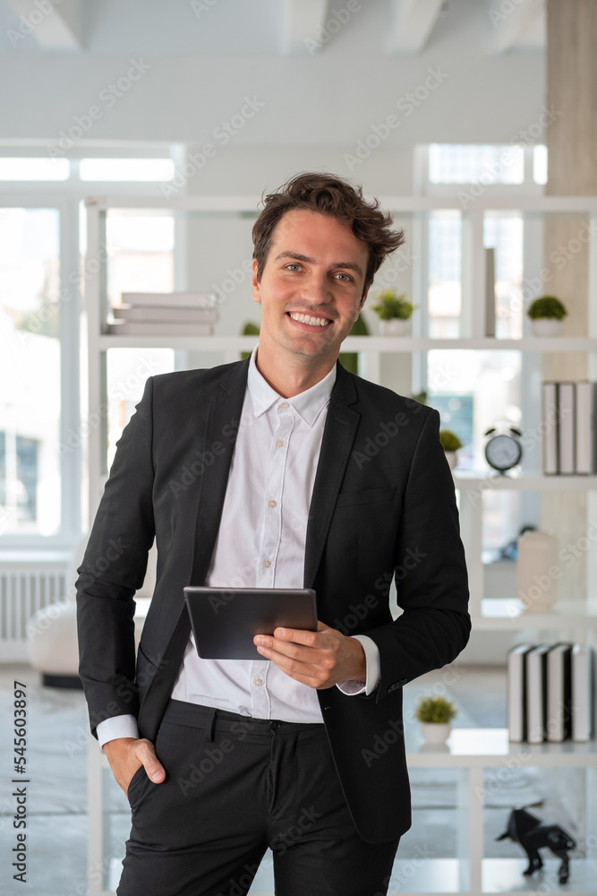 Smiling businessman is standing holding tablet device looking at camera Smiling businessman is standing holding tablet device looking at camera