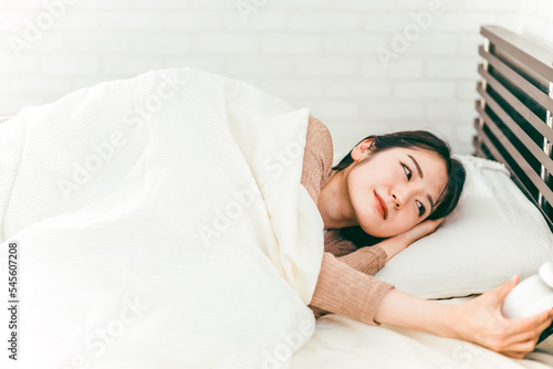 ベッドで眠くて寝ぼけながら目覚まし時計を止める低血圧の日本人女性
 photo