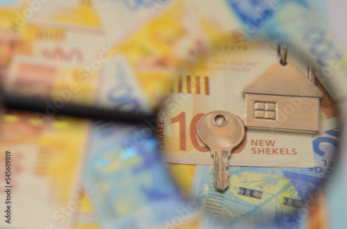 Israeli shekel banknotes and a key with a house keychain, a magnifying glass. Concept: buying real estate in Israel, renting a house, mortgage loan. photo