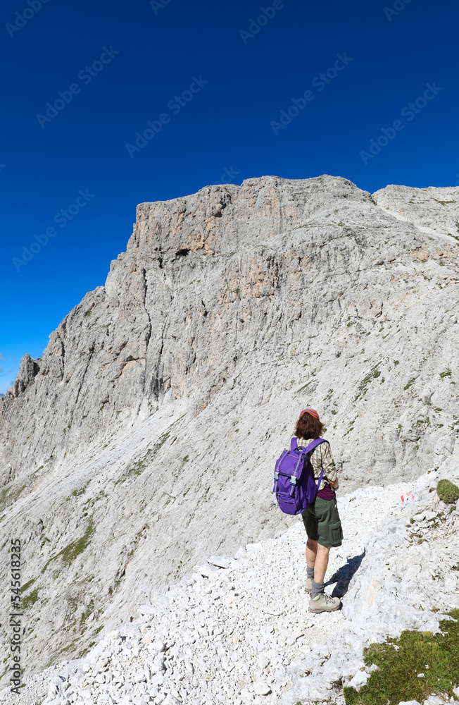 woman with backpack walks on the gravel path in the italian alps