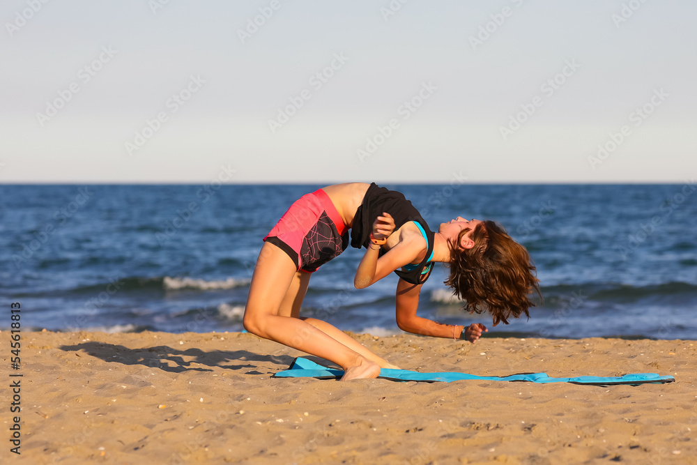 Fototapeta premium young girl does exercises on the beach by the sea