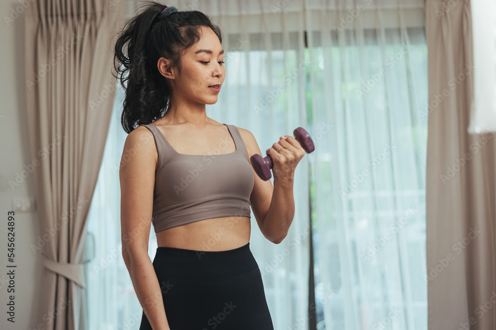 Asian woman exercise at home. Healthy female in sportswear workout training with dumbbell in living room, Health care and wellness concept.